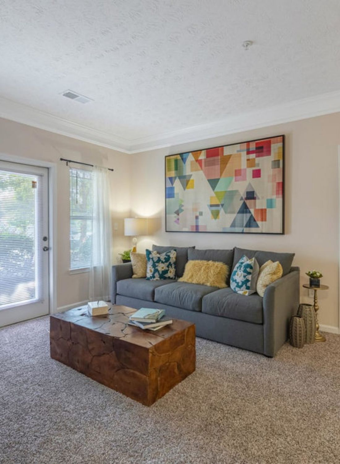 Bright living room with a gray sofa, abstract art, wooden coffee table, and open doorway to a bedroom.