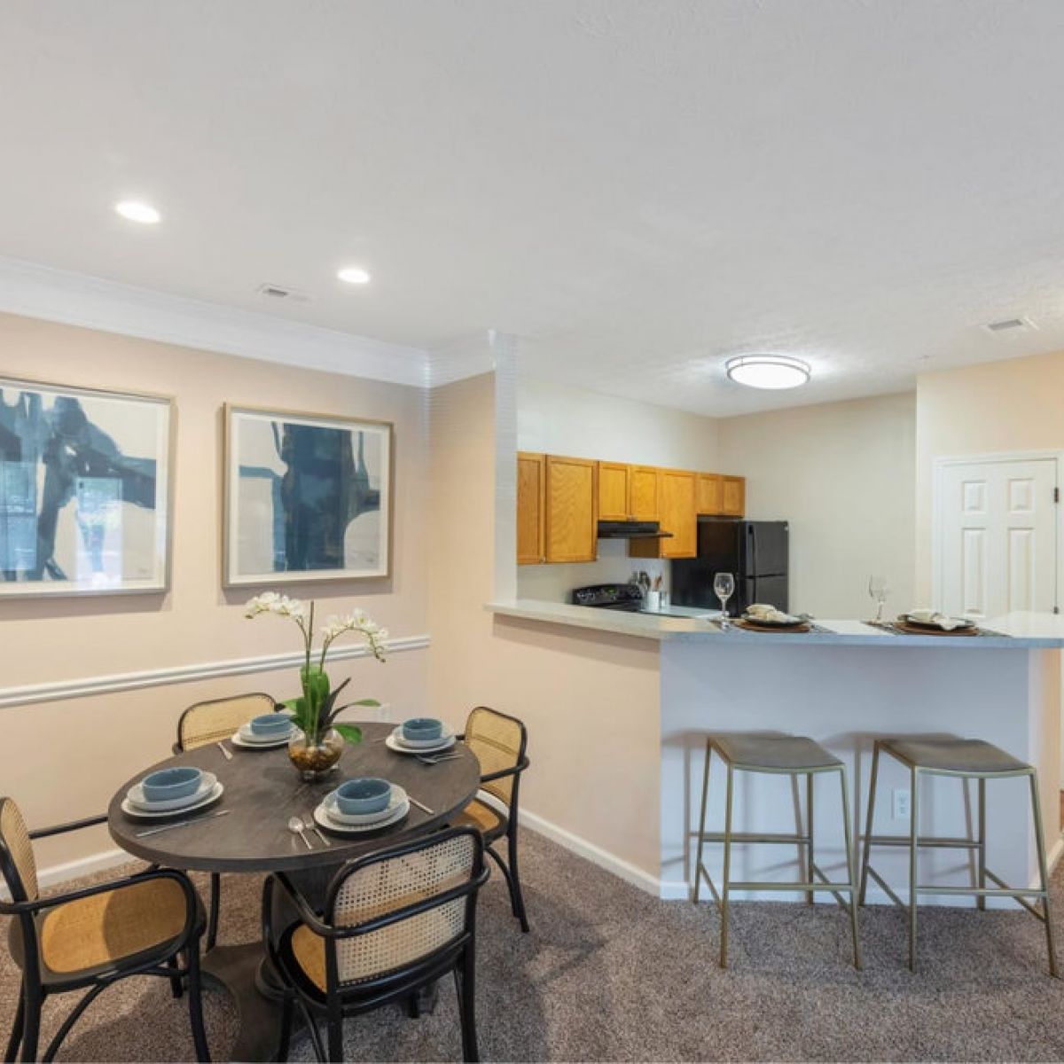 A modern dining area with a round table, four chairs, and a kitchen with a breakfast bar and stools.