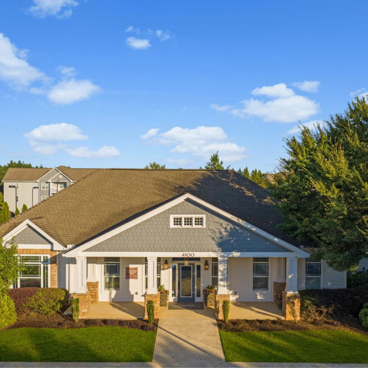 Single-story building with a gray roof, white trim, and a covered entry, surrounded by trees and shrubs.