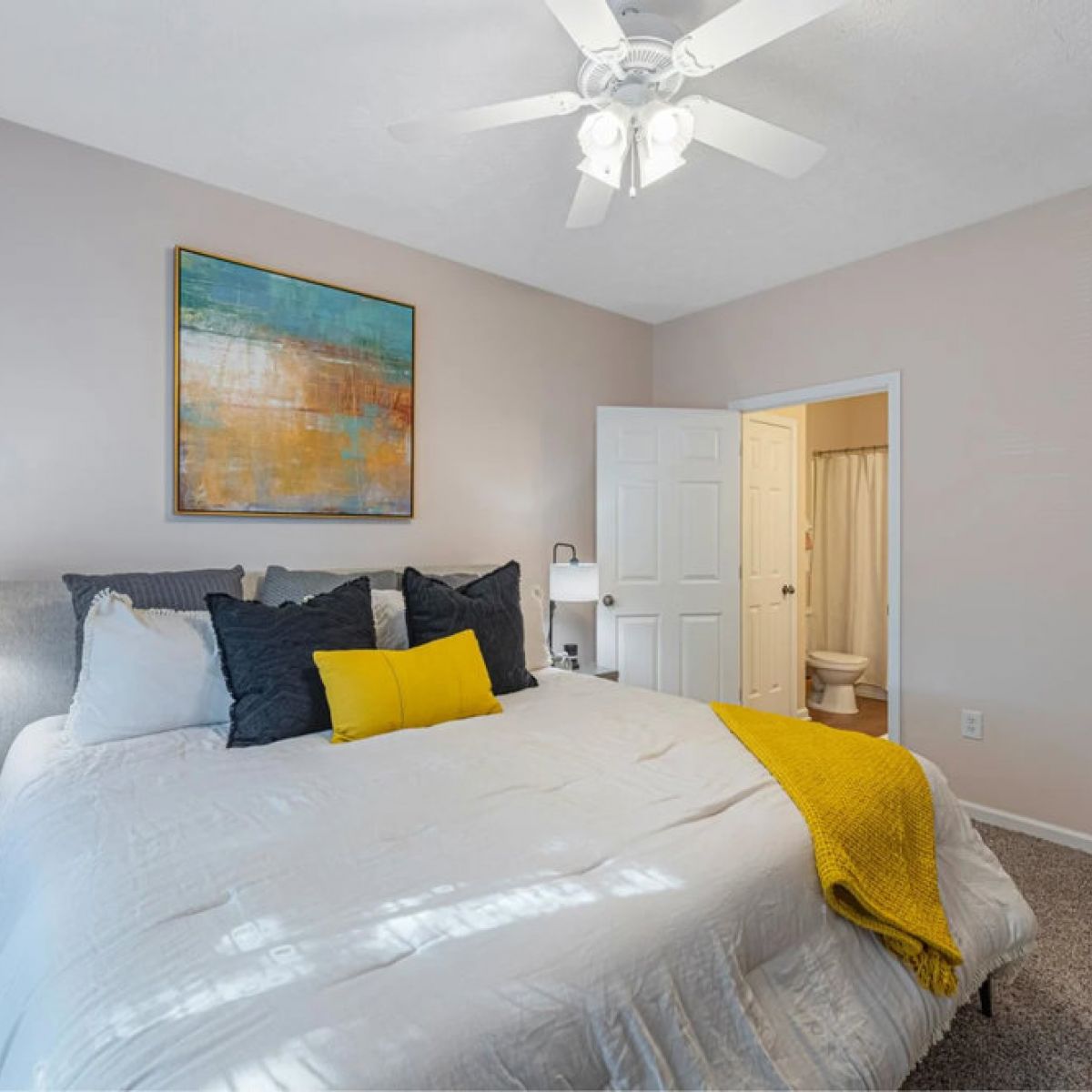 Bright bedroom with white bed, yellow accents, abstract wall art, and doorways to bathroom and walk-in closet.