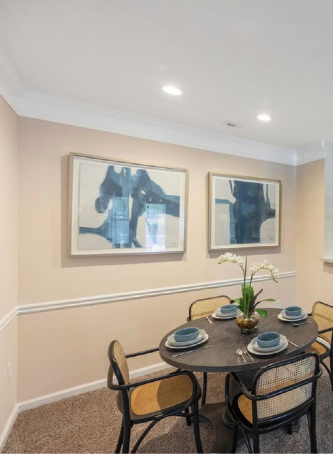 A modern dining area with a round table, four chairs, and a kitchen with a breakfast bar and stools.