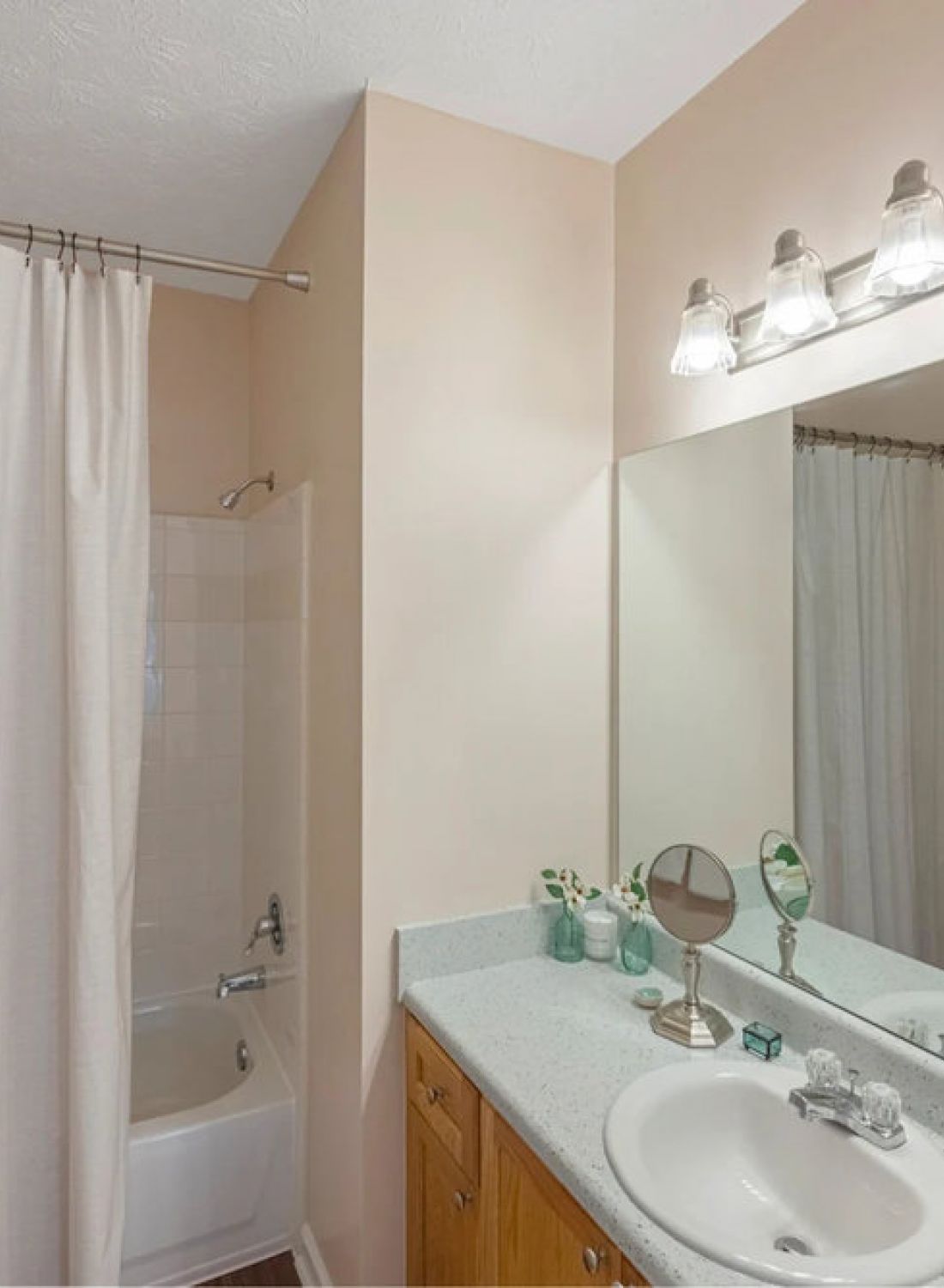 Bathroom with a shower curtain, vanity with sink, mirror, wall lights, and art above a toilet with towels.