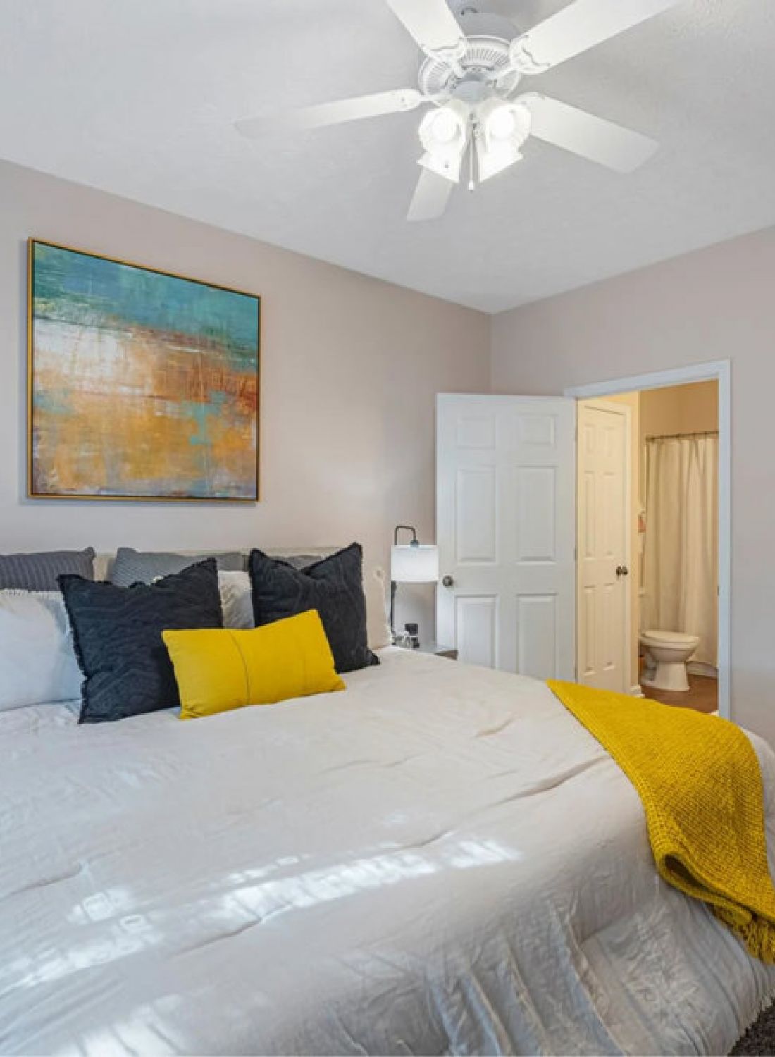Bright bedroom with white bed, yellow accents, abstract wall art, and doorways to bathroom and walk-in closet.