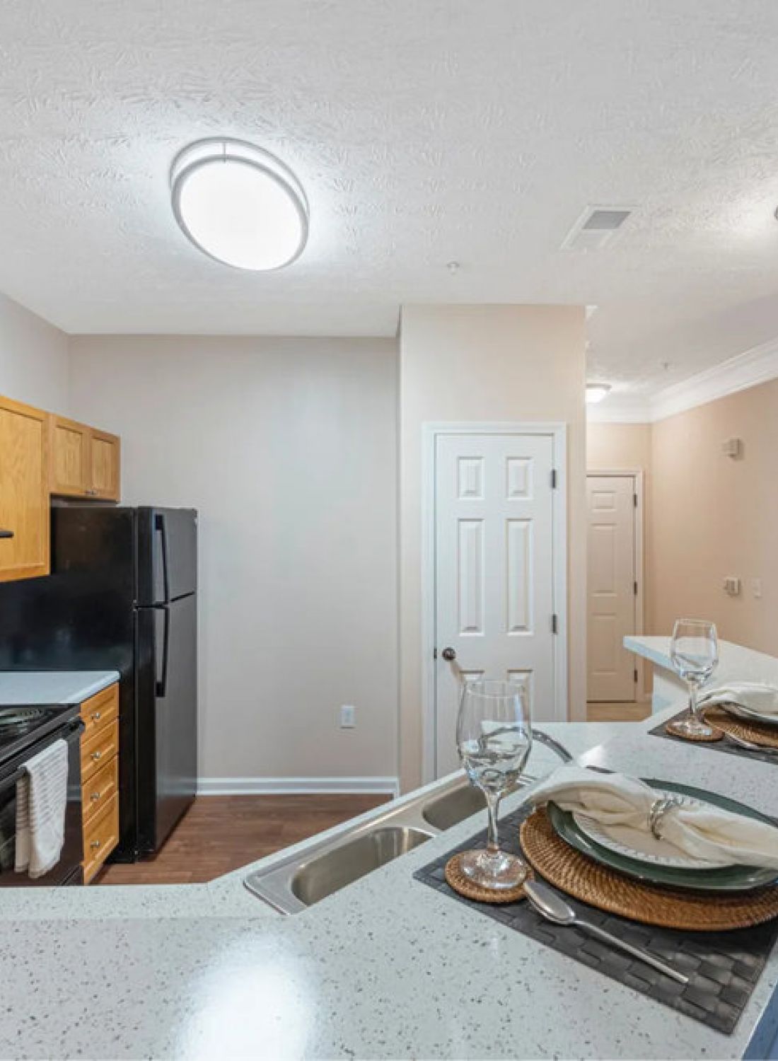 Modern kitchen with wood cabinets, black appliances, and a breakfast bar set for two with plates and glasses.